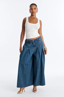 Stylish woman models a white ribbed tank top and dark blue wide-leg pleated jeans.